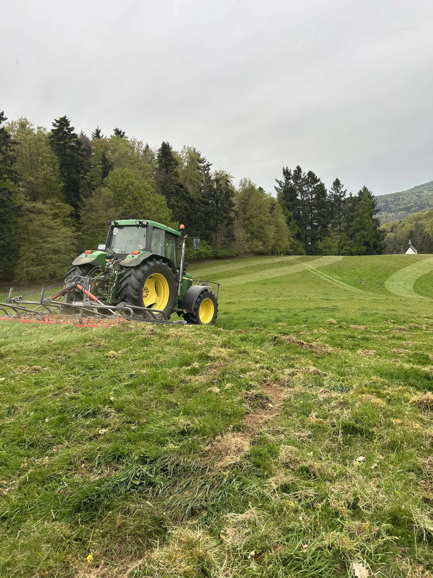 Traktor bei der Wiesenpflege auf dem Basilishof Ein Traktor arbeitet auf einer Wiese, umgeben von Bäumen und Hügeln.