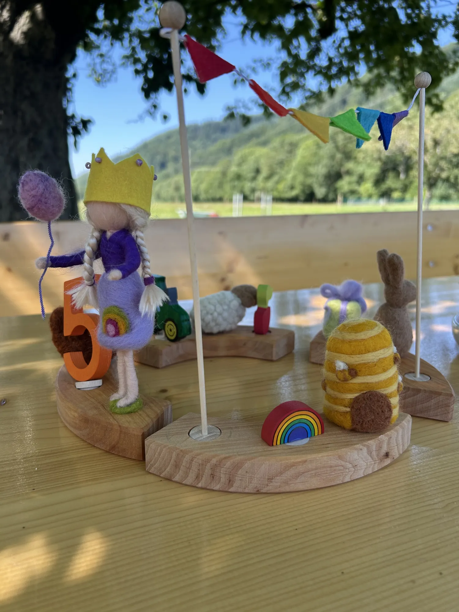 Eine kleine Holzfigur mit Krone steht neben einer orangefarbenen Zahl 5, umgeben von Filztieren und Deko auf einem Holztisch.