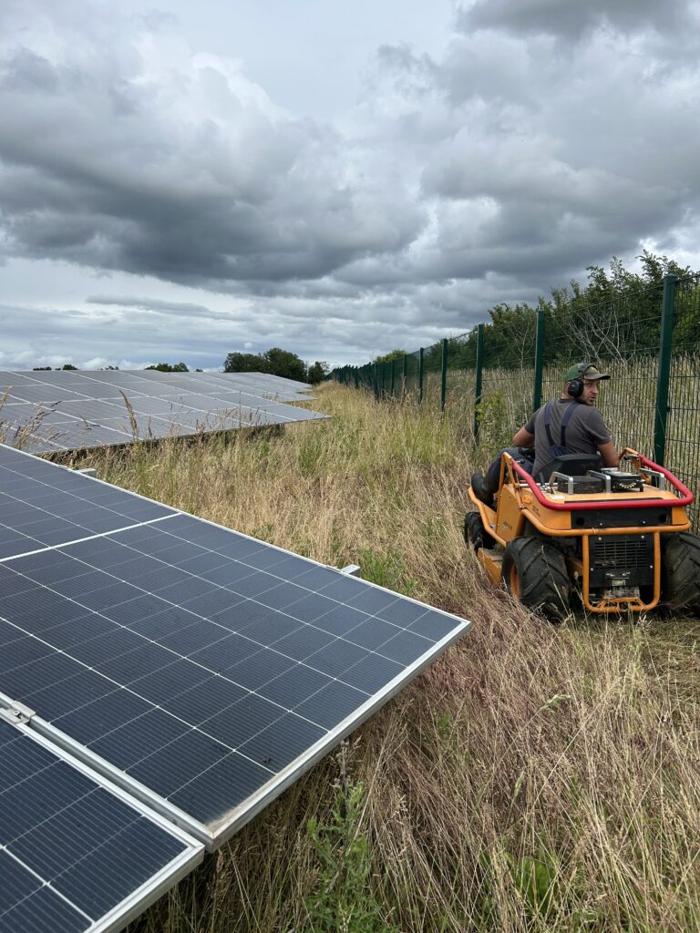In einem Solarpark mäht Mann mit einem AS-Hochgrasmäher den Randbereich am Zaun.